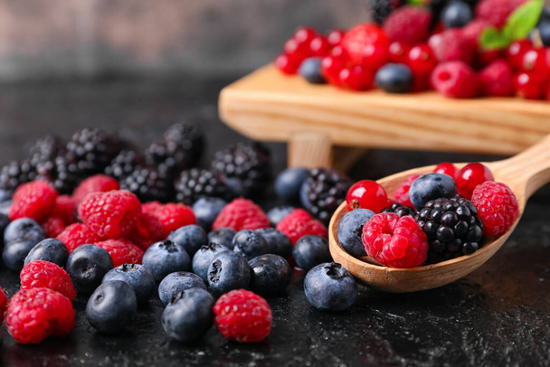Ложка и поднос с различными вкусными ягодами на темном фоне - Фото, изображение