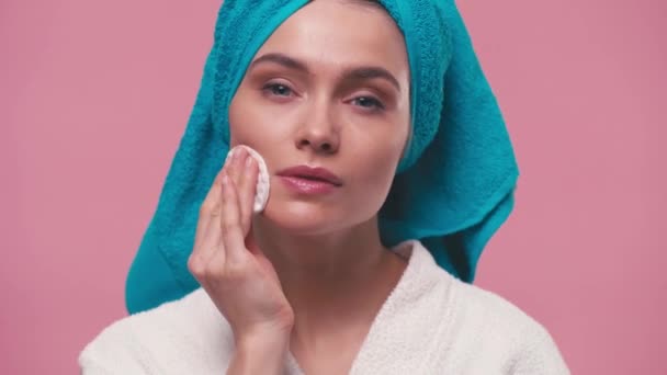 Cara de limpieza de mujer joven con almohadilla de algodón aislada en rosa - Metraje, vídeo
