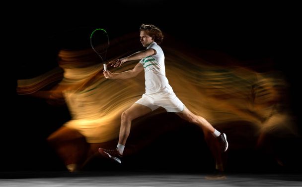 Young caucasian professional sportsman playing tennis on black background in mixed light - Foto, Imagen