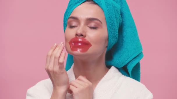 young woman with towel on head applying lip mask isolated on pink - Séquence, vidéo