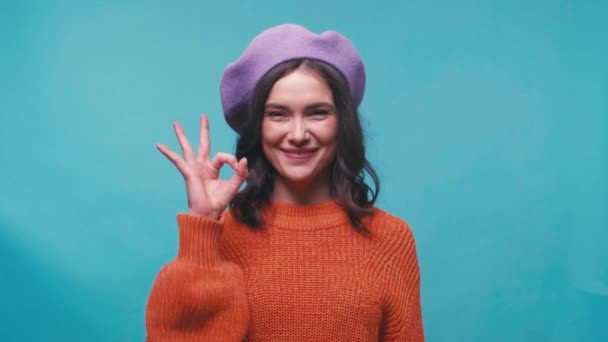 glückliche Frau in Baskenmütze zeigt Okay Zeichen isoliert auf blau - Filmmaterial, Video