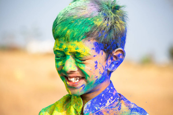 Mosolygós, fiatal arckép a holi fesztiválszíneket viselő gyerekről - Fotó, kép