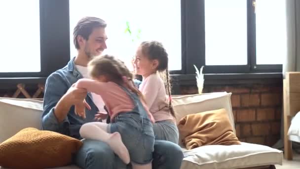 Χαρούμενη οικογένεια κόρες και ο μπαμπάς διασκεδάζουν γελώντας ξαπλωμένοι στον καναπέ μαζί - Πλάνα, βίντεο