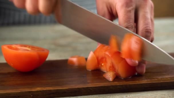 Шеф-повар режет спелый красный помидор острым ножом на доске. Крупный план - Кадры, видео