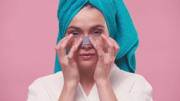 junge Frau trägt Kosmetikpflaster auf Nase isoliert auf rosa auf - Filmmaterial, Video