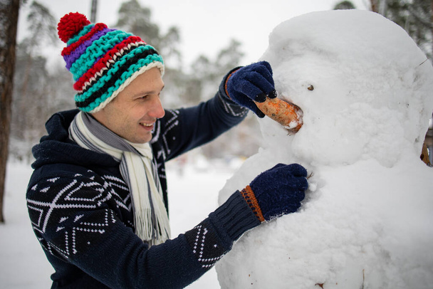 Man Vrolijke hippe gebreide hoed en warme handschoenen spelen met sneeuwpop sneeuw - Foto, afbeelding