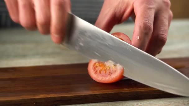 El chef está cortando un tomate rojo maduro con un cuchillo afilado en una tabla de cortar. Primer plano. - Metraje, vídeo