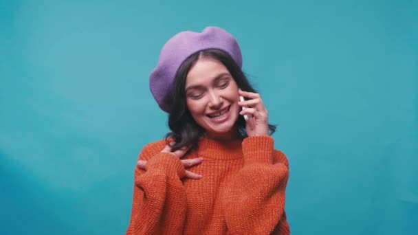 boldog nő svájcisapkában beszél okostelefon elszigetelt kék - Felvétel, videó