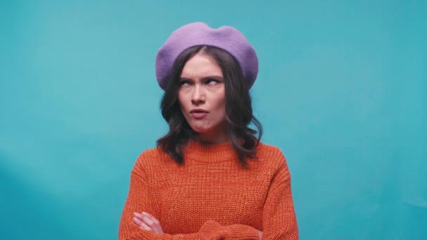 beledigde vrouw in baret staand met gekruiste armen geïsoleerd op blauw - Video