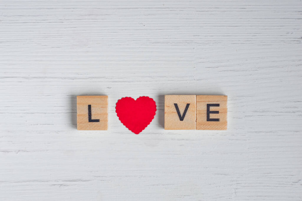 Top view of the word love laid out from square wooden tiles and smal red hearts on old white wooden background. Concept of valentine day. - Foto, Imagem