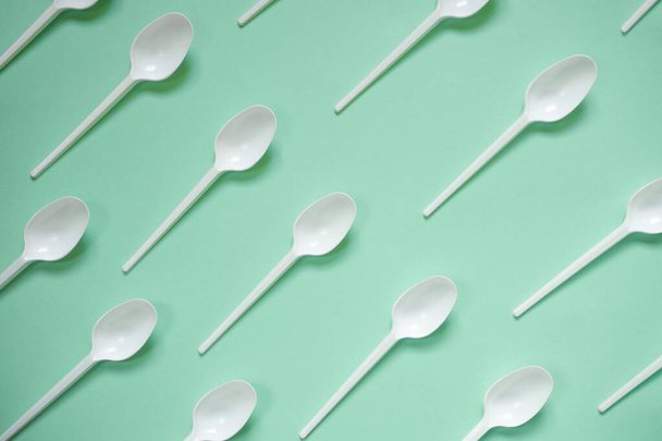 Disposable picnic white plastic spoon diagonally on a green background. View from above. Flat lay. Paternn. Disposable plastic recycling concept. Template. Zero waste, save the planet, plastic hazard. Trendy color - 写真・画像
