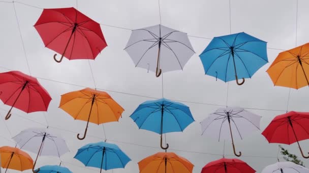 Πολύχρωμες ομπρέλες κρέμονται πάνω από συννεφιασμένο ουρανό σε υπαίθριο φεστιβάλ: αργή κίνηση - Πλάνα, βίντεο