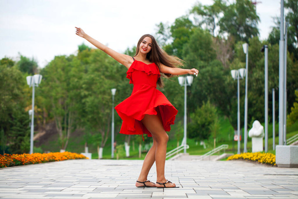 Portrait in full growth, young beautiful brunette woman in red dress walking on the street, summer embankment outdoors - Valokuva, kuva