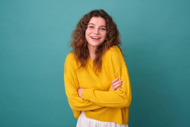 Happy joyful woman laughs happily keeps her hands folded on her chest and expresses positive emotions smiles with happiness dressed in a casual yellow jumper isolated on a blue background having fun - Foto, immagini