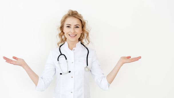Family doctor and healthcare concept. Panoramic view of happy medic wearing in white coat with stethoscope, gesturing with hands, choosing options and showing balance against copy space wall - Photo, Image