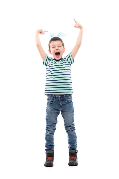 Χαρούμενο ενθουσιασμένο παιδί με αυτιά πασχαλινού κουνελιού να δείχνουν προς τα πάνω και να ουρλιάζουν. Πλήρες μήκος απομονωμένο σε λευκό φόντο. - Φωτογραφία, εικόνα