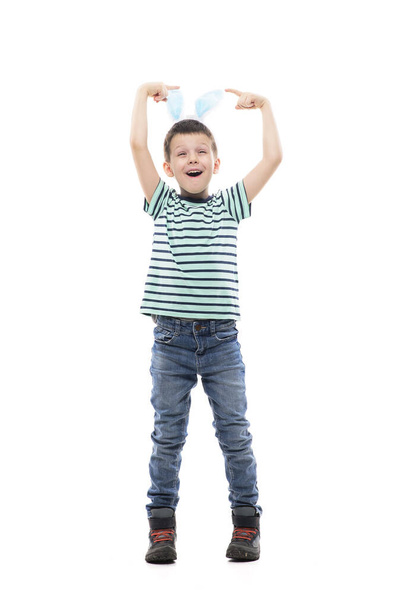 Χαρούμενο ενθουσιασμένο νεαρό αγόρι με αυτιά κουνελιού που γιορτάζει το Πάσχα διασκεδάζοντας. Πλήρες μήκος απομονωμένο σε λευκό φόντο. - Φωτογραφία, εικόνα