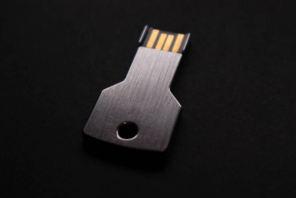 USB-flashstation in de vorm van een sleutel, die de gegevensbescherming symboliseert. Zwarte achtergrond - Foto, afbeelding