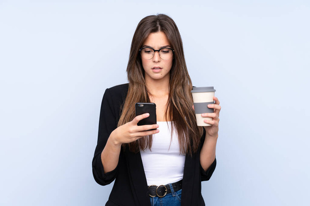 Junge brasilianische Geschäftsfrau hält Kaffee zum Mitnehmen vor isoliertem blauen Hintergrund - Foto, Bild