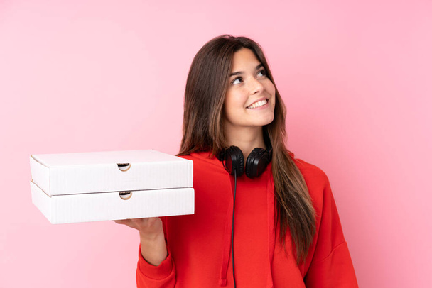Adolescente brasileña sosteniendo cajas de pizza sobre una pared rosa aislada mirando hacia arriba mientras sonríe - Foto, imagen