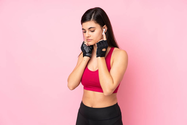 Joven mujer del deporte sobre fondo rosa aislado escuchando música - Foto, imagen