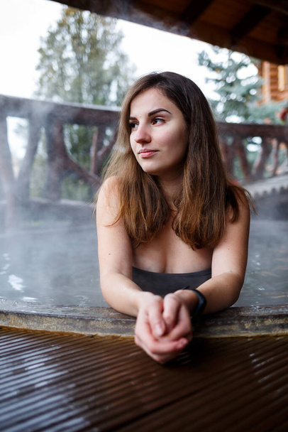 Girl in the pool with hot water on the terrace, spa body treatments. Relax in the open air, wellness. Cottage with spa bath. Outdoor Jacuzzi. Jacuzzi with a girl. Beautiful figure woman in a swimsuit - Fotó, kép