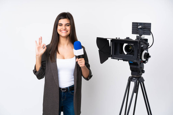 Reportérka drží mikrofon a hlásí zprávy nad izolovaným bílým pozadím, na kterém je ukazatel "ok" s prsty - Fotografie, Obrázek