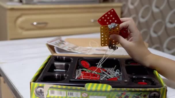 Περίεργο αγόρι παίζει με μεταλλικά μέρη του κατασκευαστή στο τραπέζι στο σπίτι. 4K - Πλάνα, βίντεο