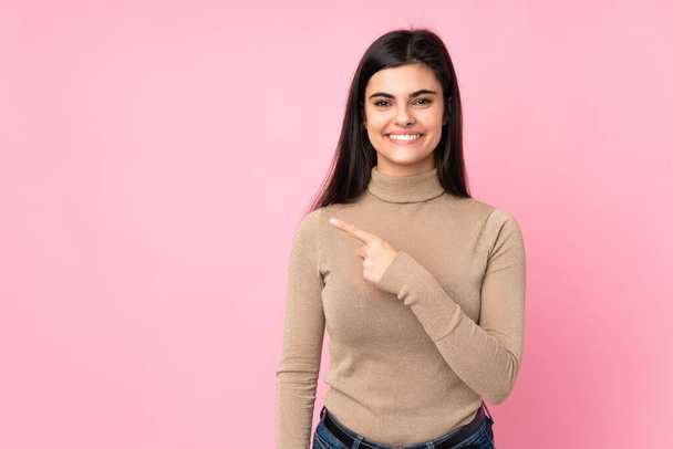 Young woman over isolated pink background pointing to the side to present a product - Foto, afbeelding