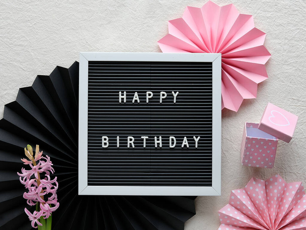 Text Happy Birthday on letter board, letterboard. Creative flat lay in pink and black on cream white textile. Party decor, paper fans, sugar hearts and pink gift box. - Valokuva, kuva