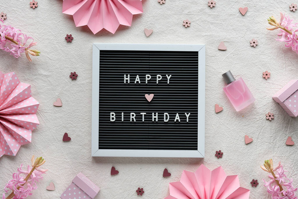 Text Happy Birthday on letter board, letterboard. Creative flat lay, top view on ivory, off white textile. Party decor, paper fans, gift boxes, hearts. Natural pink hyacinth flowers, perfume. - Fotó, kép