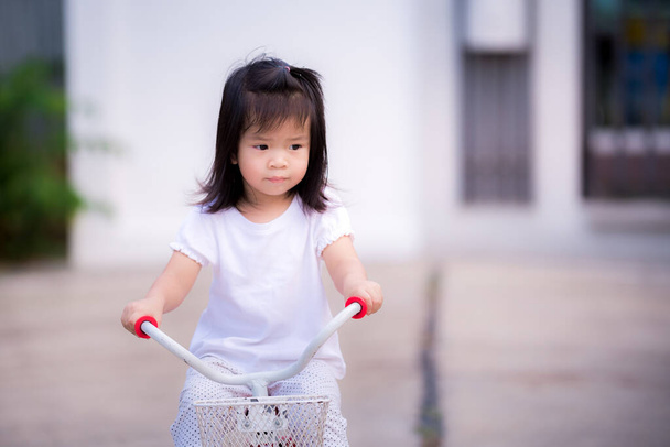 Girl is sadly riding bicycle from social distancing in epidemic pneumonia situation. She doesn't have friends of the same age to run around and talk to. Asian children lonely and depressed. - Photo, Image