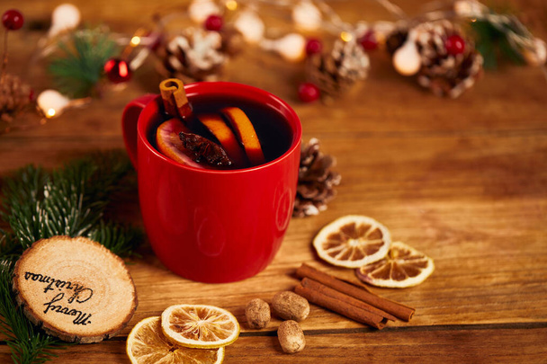 A red mug of tea with citrus and cinnamon on wooden table with dry lemon slices and Christmas decors - 写真・画像