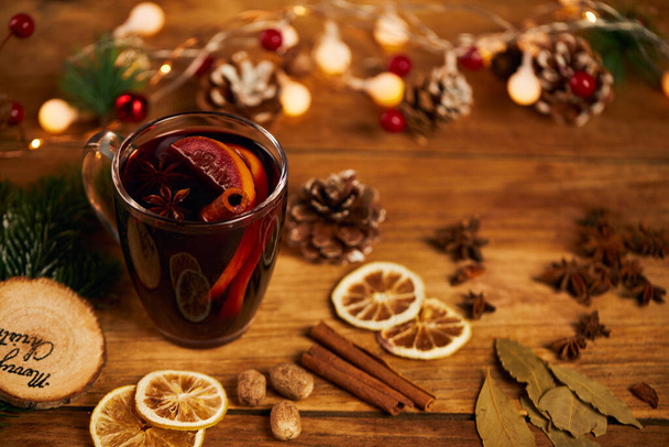A cup of hot tea with citrus and cinnamon on wooden table with dried lemon slices and Christmas decors - Photo, Image