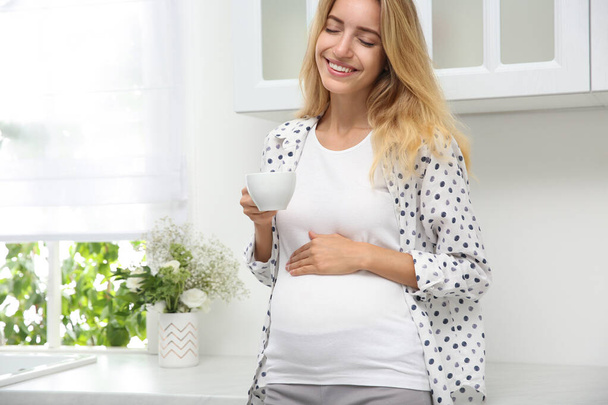 Beautiful pregnant woman drinking tea in kitchen - 写真・画像
