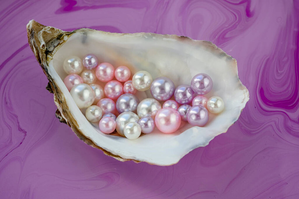 Künstliche Perlen in der Austernschale. Verschiedene Farben und Größen der Perlen. Isoliert auf rosa Hintergrund  - Foto, Bild