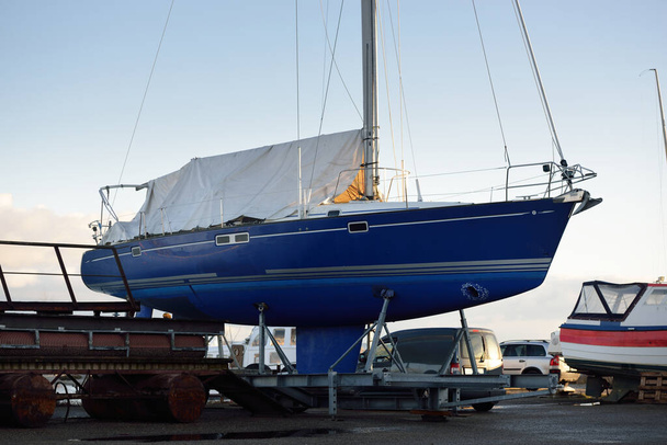 Kék sloop manipulált jacht áll a szárazföldön egy kis kikötőben egy tiszta téli napon. Várom az új vitorlás szezont. Ipar, üzlet, közlekedés, szolgáltatás, logisztika, sport, szabadidős koncepciók - Fotó, kép
