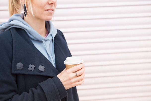 Close up photo of a young blond woman in casual clothes holding and drinking cup of coffee. Pale rose color wall background. Copy space area. - Foto, Bild