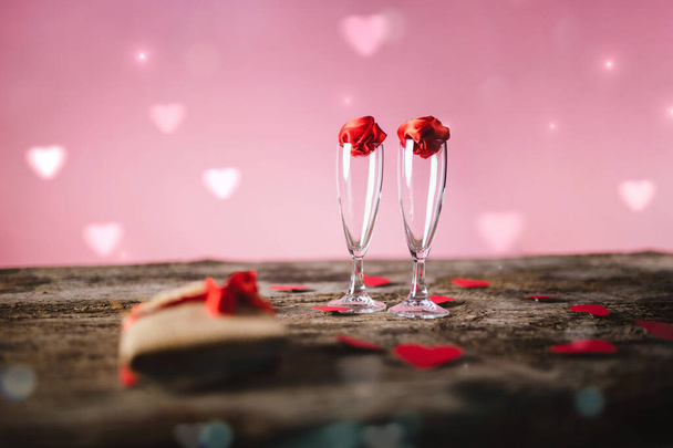 İki bardak ahşap masada kırmızı güller ve kırmızı kalpler - Fotoğraf, Görsel