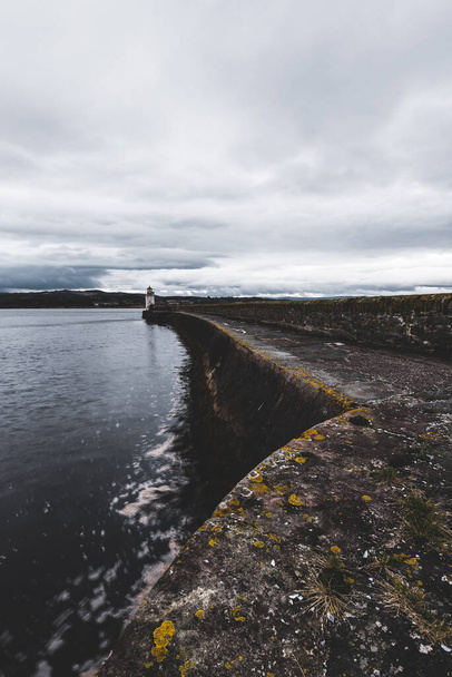 Une promenade vide vers le vieux phare, gros plan. Des rivages rocheux en arrière-plan. Paysage nuageux dramatique. Ardrishaig, canal de Crinan, Écosse, Royaume-Uni. Destinations touristiques, thème touristique - Photo, image