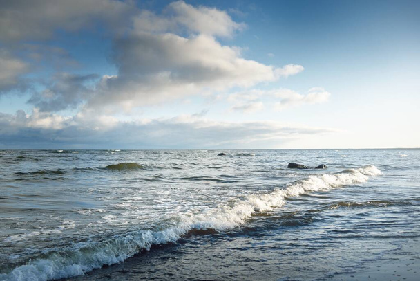 Blick auf die Ostsee im Winter. Klarer blauer Himmel mit glühenden Kumuluswolken. Oberflächenstruktur des Wassers, Wellen und Wasserspritzer aus nächster Nähe. Wetterkapriolen, Klimawandel, Natur, Meereslandschaft - Foto, Bild