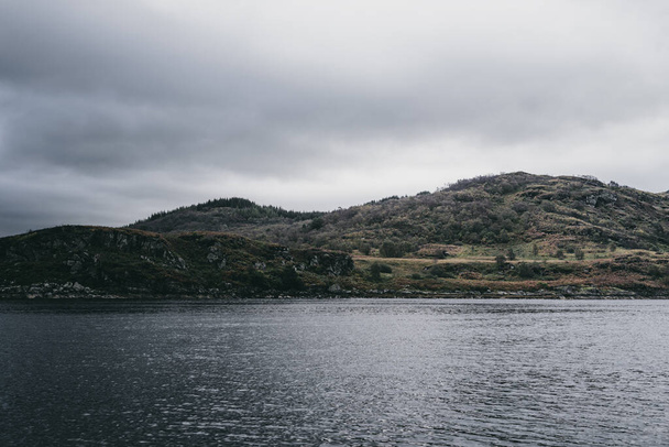Plavit se poblíž skalnatých břehů Kyles of Bute za oblačného dne. Skotsko, Velká Británie. Dramatické bouřlivé nebe. Cestovní destinace, národní památky, cestovní ruch, dovolená, koncepce volnočasových aktivit - Fotografie, Obrázek