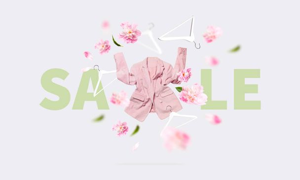 Spring sale Springtime discounts. Womens fashionable flying pink blazer flowers peonies white wooden hanger on gray background. Creative clothing concept shopping. Female stylish fabric cotton jacket. - Photo, Image