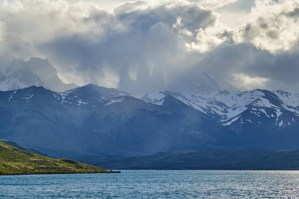 Tours du parc national des torres del Paine couvertes de nuages avec forêt vert foncé un lac et des montagnes enneigées des Andes en Patagonie sud du Chili - Photo, image
