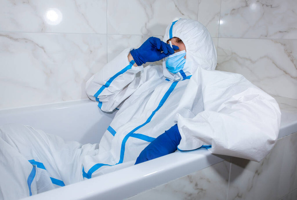 Médico con traje de protección médica, máscara y guantes acostado en el baño. Relájate después del trabajo. Marineros de protección por epidemia de virus. Coronavirus (COVID-19). Concepto sanitario. - Foto, imagen