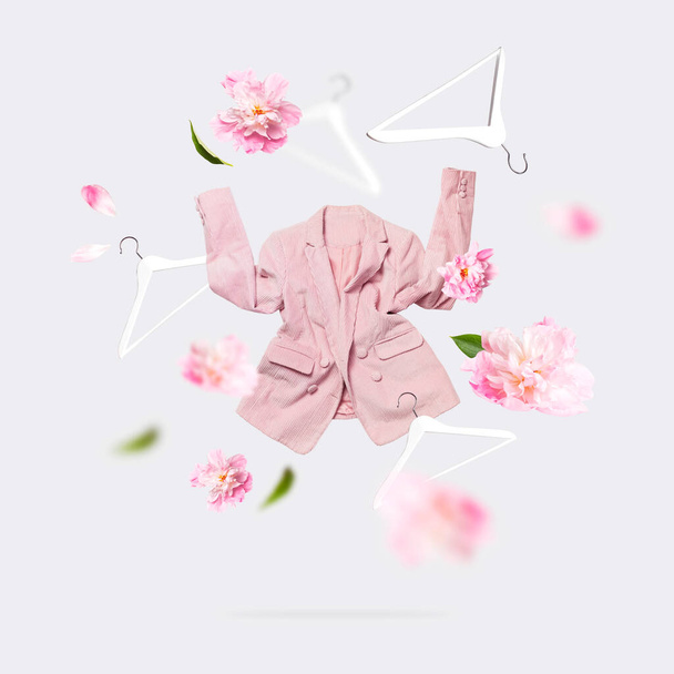 Концепція творчого весняного одягу. Жіночі модні літаючі рожеві квіти блейзера півонії біла дерев'яна вішалка на сірому фоні. Жіноча мода, стильна тканина бавовняна куртка. Продаж, весняні знижки
. - Фото, зображення