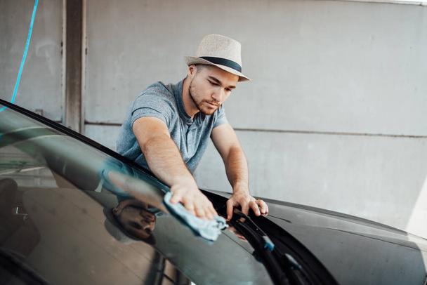Young handsome man with hat cleaning car with rag, car detailing (or valeting) concept.  - Φωτογραφία, εικόνα