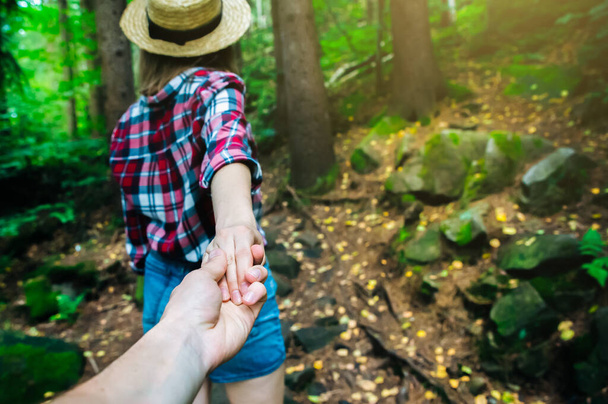 山の中で写真を撮ってください。チェック柄のシャツと藁帽子のスタイリッシュな女性。欲望の概念。カップルハイキングや夏に旅行。自然の中で手を握る. - 写真・画像