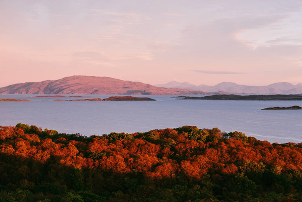 Panoramic aerial view of the isles of Jura and Mull at sunrise. Pure morning sunlight above the rocky shores, forest and hills. Glowing pink clouds. Loch Craignish, Crinan Canal, Scotland, UK - Photo, Image