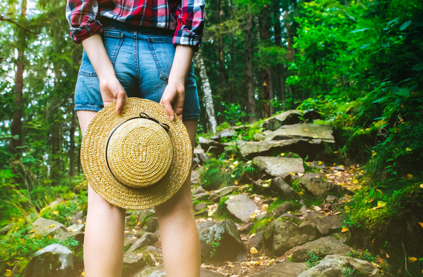 Hipster girl in the mountains. Stylish woman in straw hat and checkered shirt in forest. Wanderlust concept. Freedom and psychology concept. Beautiful nature. - 写真・画像